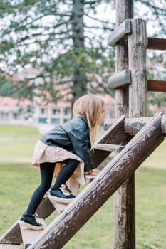 Little girl climbs the wooden stairs on the playground in the park. Side view. High quality photo