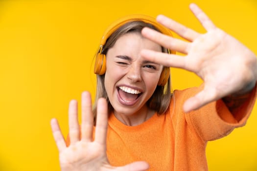 Happy emotions concept. Positive and beautiful young woman laughs poisitively looks aside with carefree face expression wears casual orange sweater isolated over yellow studio background.