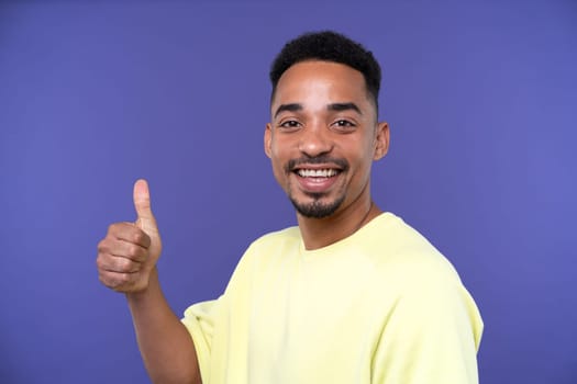 Emotional young black guy in casual raising fists up studio background, celebrating success, happy handsome african american millennial man sharing good emotions, copy space