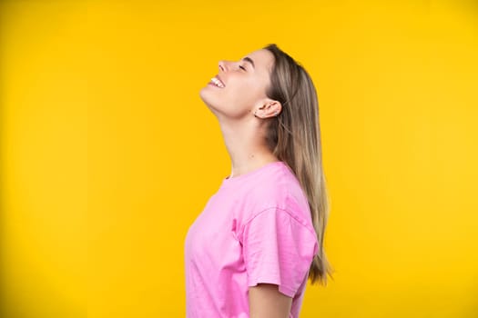 Happy emotions concept. Positive and beautiful young woman laughs poisitively looks aside with carefree face expression wears casual orange sweater isolated over yellow studio background.