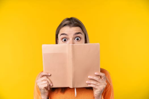 Happy emotions concept. Positive and beautiful young woman laughs poisitively looks aside with carefree face expression wears casual orange sweater isolated over yellow studio background.