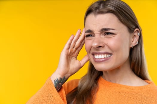 Happy emotions concept. Positive and beautiful young woman laughs poisitively looks aside with carefree face expression wears casual orange sweater isolated over yellow studio background.