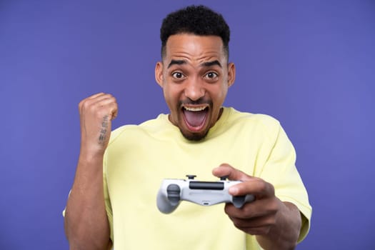 Emotional young black guy in casual raising fists up studio background, celebrating success, happy handsome african american millennial man sharing good emotions, copy space