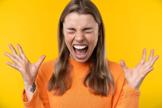 Happy emotions concept. Positive and beautiful young woman laughs poisitively looks aside with carefree face expression wears casual orange sweater isolated over yellow studio background.