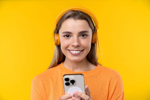 Happy emotions concept. Positive and beautiful young woman laughs poisitively looks aside with carefree face expression wears casual orange sweater isolated over yellow studio background.