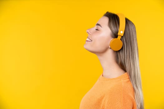 Happy emotions concept. Positive and beautiful young woman laughs poisitively looks aside with carefree face expression wears casual orange sweater isolated over yellow studio background.