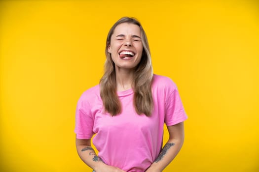 Happy emotions concept. Positive and beautiful young woman laughs poisitively looks aside with carefree face expression wears casual orange sweater isolated over yellow studio background.