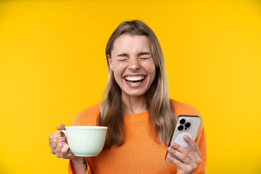 Happy emotions concept. Positive and beautiful young woman laughs poisitively looks aside with carefree face expression wears casual orange sweater isolated over yellow studio background.