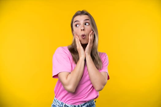 Happy emotions concept. Positive and beautiful young woman laughs poisitively looks aside with carefree face expression wears casual orange sweater isolated over yellow studio background.