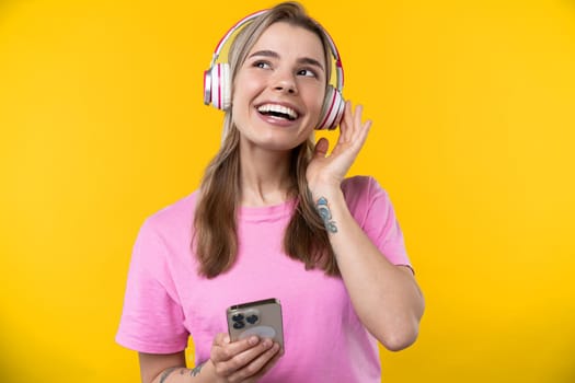 Happy emotions concept. Positive and beautiful young woman laughs poisitively looks aside with carefree face expression wears casual orange sweater isolated over yellow studio background.