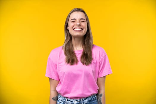 Happy emotions concept. Positive and beautiful young woman laughs poisitively looks aside with carefree face expression wears casual orange sweater isolated over yellow studio background.