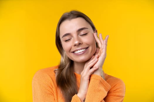 Happy emotions concept. Positive and beautiful young woman laughs poisitively looks aside with carefree face expression wears casual orange sweater isolated over yellow studio background.