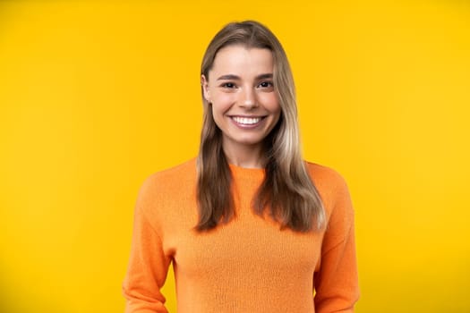 Happy emotions concept. Positive and beautiful young woman laughs poisitively looks aside with carefree face expression wears casual orange sweater isolated over yellow studio background.