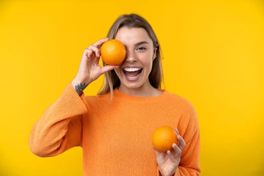 Happy emotions concept. Positive and beautiful young woman laughs poisitively looks aside with carefree face expression wears casual orange sweater isolated over yellow studio background.