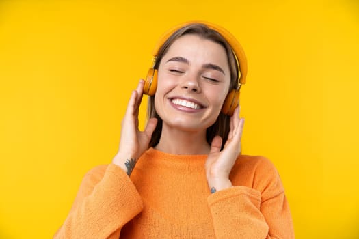 Happy emotions concept. Positive and beautiful young woman laughs poisitively looks aside with carefree face expression wears casual orange sweater isolated over yellow studio background.