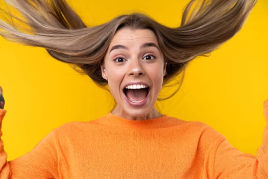 Happy emotions concept. Positive and beautiful young woman laughs poisitively looks aside with carefree face expression wears casual orange sweater isolated over yellow studio background.