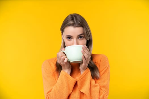 Happy emotions concept. Positive and beautiful young woman laughs poisitively looks aside with carefree face expression wears casual orange sweater isolated over yellow studio background.