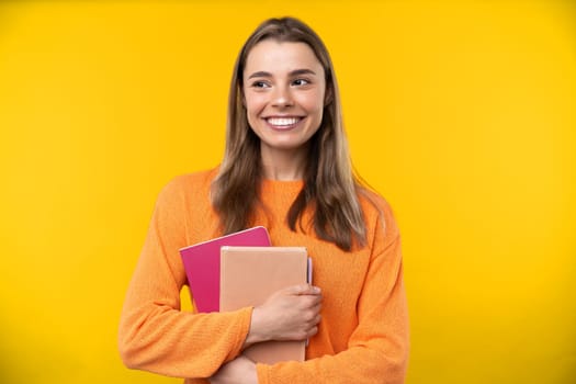 Happy emotions concept. Positive and beautiful young woman laughs poisitively looks aside with carefree face expression wears casual orange sweater isolated over yellow studio background.