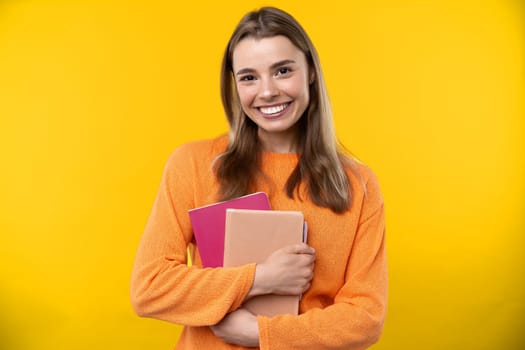 Happy emotions concept. Positive and beautiful young woman laughs poisitively looks aside with carefree face expression wears casual orange sweater isolated over yellow studio background.