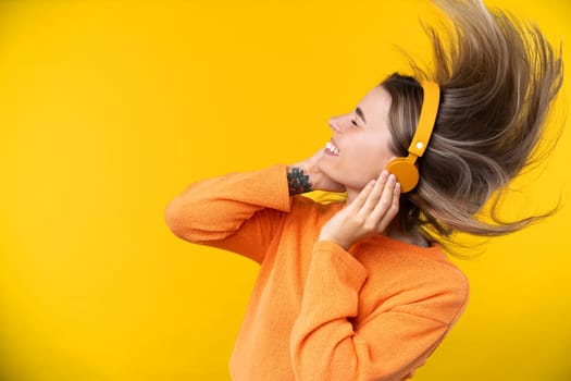 Happy emotions concept. Positive and beautiful young woman laughs poisitively looks aside with carefree face expression wears casual orange sweater isolated over yellow studio background.