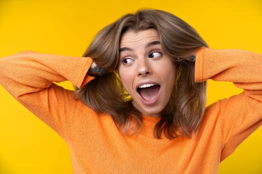 Happy emotions concept. Positive and beautiful young woman laughs poisitively looks aside with carefree face expression wears casual orange sweater isolated over yellow studio background.