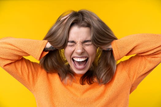 Happy emotions concept. Positive and beautiful young woman laughs poisitively looks aside with carefree face expression wears casual orange sweater isolated over yellow studio background.