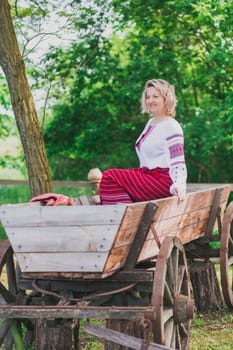 Beautiful peasant woman in embroidered Ukrainianclothes laughing near the cart.