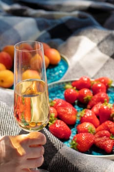 strawberries on plate with glass of champagne or white wine on picnic. Luxury lifestyle, travel concept. glass raised in hand for toast. Ripe berries. wine tasting. Vineyard. Summer fruits. aesthetics