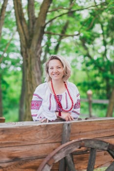Beautiful peasant woman in embroidered Ukrainian clothes laughing near the cart.