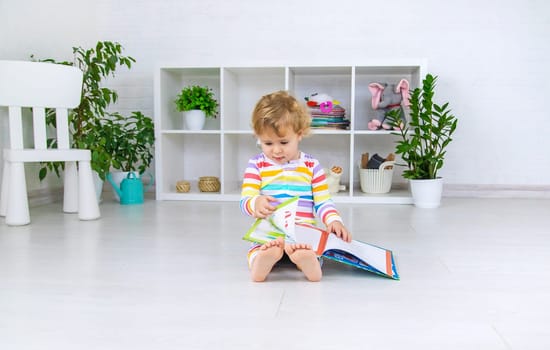 The child is looking at a book in the room. Selective focus. Baby.