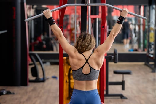 Rear view of a Caucasian forty-year-old woman doing lat pull-downs in the gym