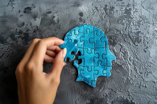 A vibrant blue jigsaw puzzle in the shape of a human head near completion on a textured surface, hand in frame