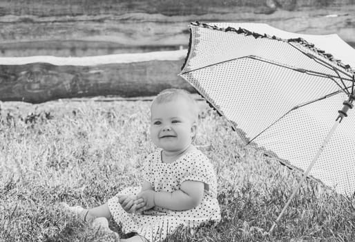beautiful baby in a polka-dot dress is sitting nea umbrella umbrella.