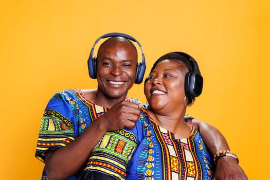 Happy african american romantic couple hugging and enjoying music sound in wireless headphones portrait. Cheerful smiling man in earphones embracing wife and looking at camera