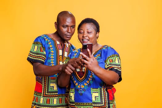 African american smiling wife showing message on smartphone to husband. Man and woman romantic couple with cheerful expression checking internet page on mobile phone together
