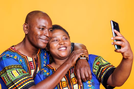 Happy african american couple smiling and hugging while taking selfie on smartphone. Cheerful boyfriend and girlfriend embracing and looking at mobile phone camera while making photo together