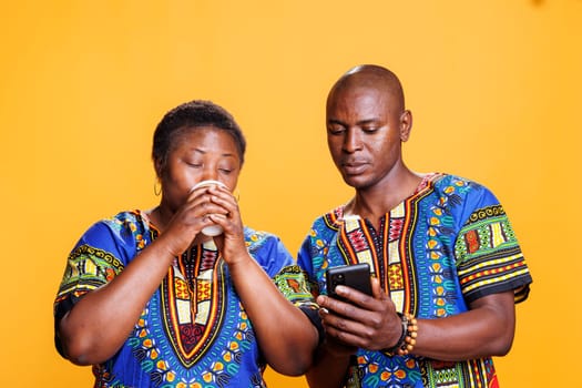 Woman drinking coffee to go while checking social media on smartphone with man. African american couple enjoying takeaway beverage and scrolling internet page on mobile phone