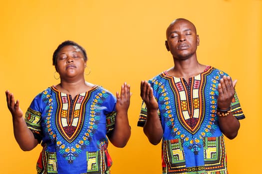 African american couple praying and asking blessing while posing with arms wide open. Religious man and woman prayers pair with closed eyes spreading hands and pleading god