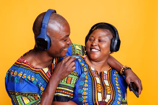 Smiling happy black man and woman pair in love wearing headphones and looking at each other with cheerful expression. Joyful boyfriend and girlfriend listening to music and hugging