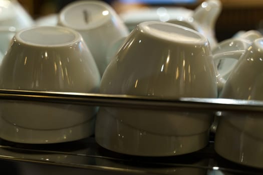 A close-up view of white coffee cups stacked neatly on a metal shelf, ready for baristas to serve warm beverages.