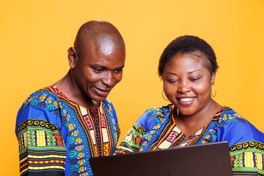 Cheerful black man and woman with smile on face using laptop and enjoying internet leisure activity together. Smiling couple using portable computer, checking information online