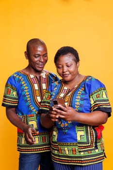Joyful spouse scrolling through social media feed on smartphone with cheerful expression. Smiling mid adult boyfriend and girlfriend holding mobile phone and enjoying online entertainment