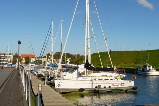 Klaipeda, Lithuania - August 11, 2023: A group of sailboats are securely moored at a marina, with their masts tall and sails neatly furled. The calm waters reflect the clear sky above, creating a picturesque scene of boating activity.