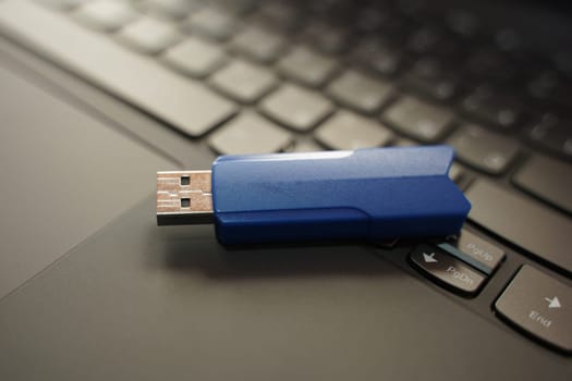 A blue USB device is placed on top of an open laptop on a desk.