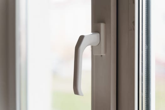 A sharp focus on a white window handle with soft natural light filtering through the glass, indicating a daytime setting.