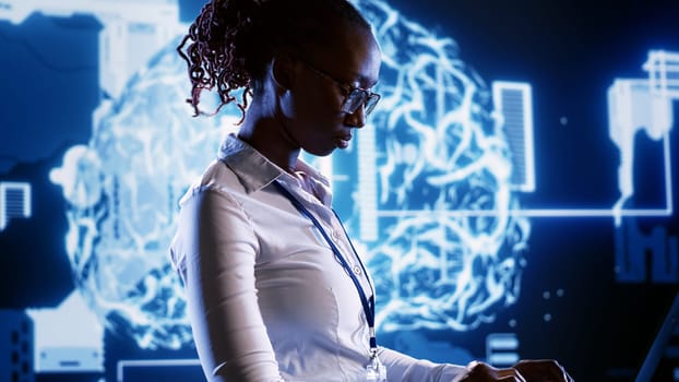 African american woman writing artificial intelligence script code in startup workspace on laptop terminal. Hardworking employee doing maintenance work in high tech facility updating AI systems