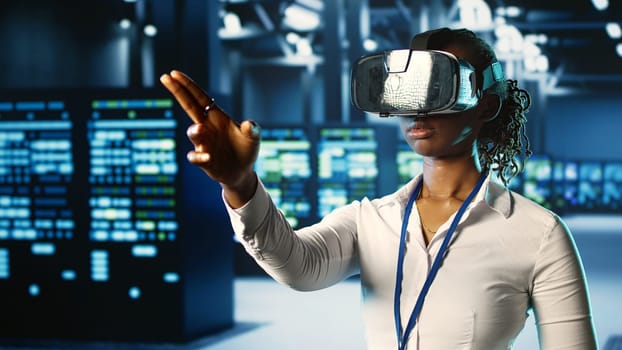 African american certified developer immersed in virtual reality at data center, doing units maintenance. Licensed technician using VR headset to optimize servers performance, checking operations