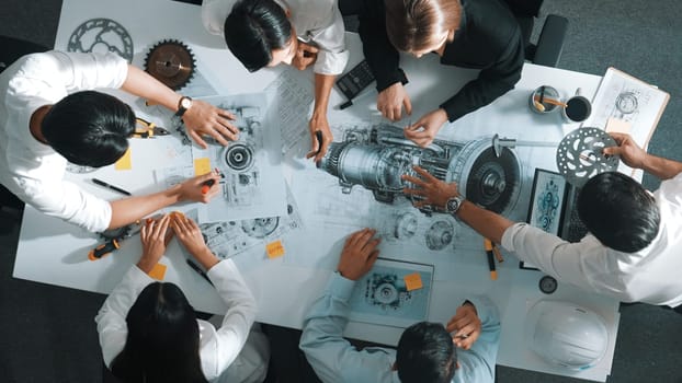 Top down aerial view of smart engineer team working together to design turbine engine. Professional technician discussing about jet engine construction while pointing at part of engine. Alimentation.