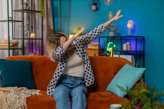 Trendy cheerful positive young woman having fun dancing, dabbing raising hands making dub winner dance gesture celebrating victory at home apartment. Excited Caucasian girl making dub dance gesture.