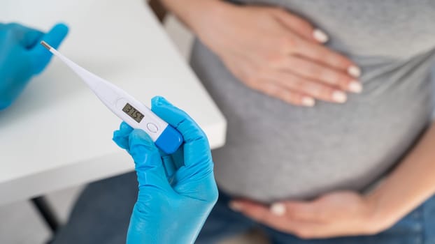 Pregnant woman with fever at doctor's appointment. Therapist holds an electronic thermometer with a temperature of 37.5